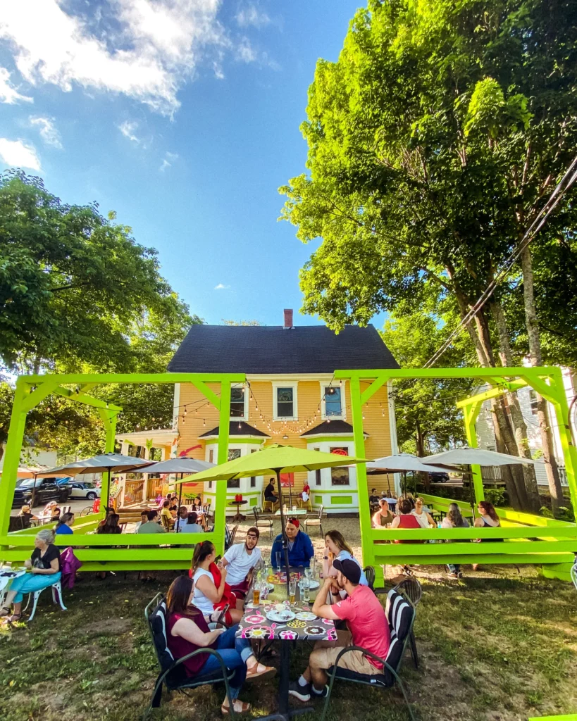 Guests at a long table on the patio in summer, the yellow house behind