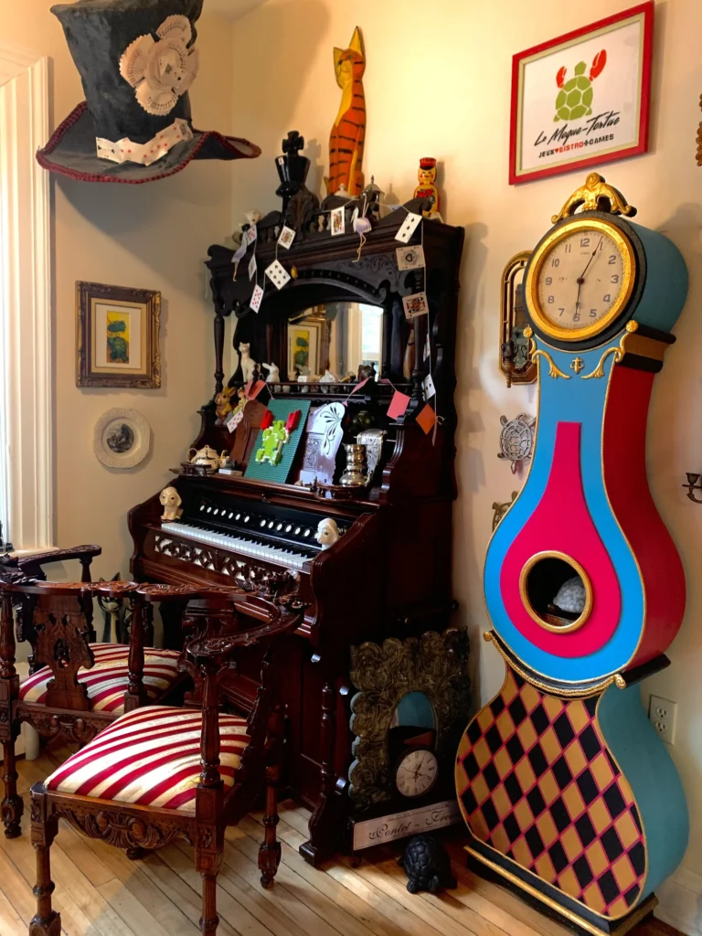 A carved antique organ, a tall painted clock, and a harlequin chair in the dining room at Le Moque-Tortue